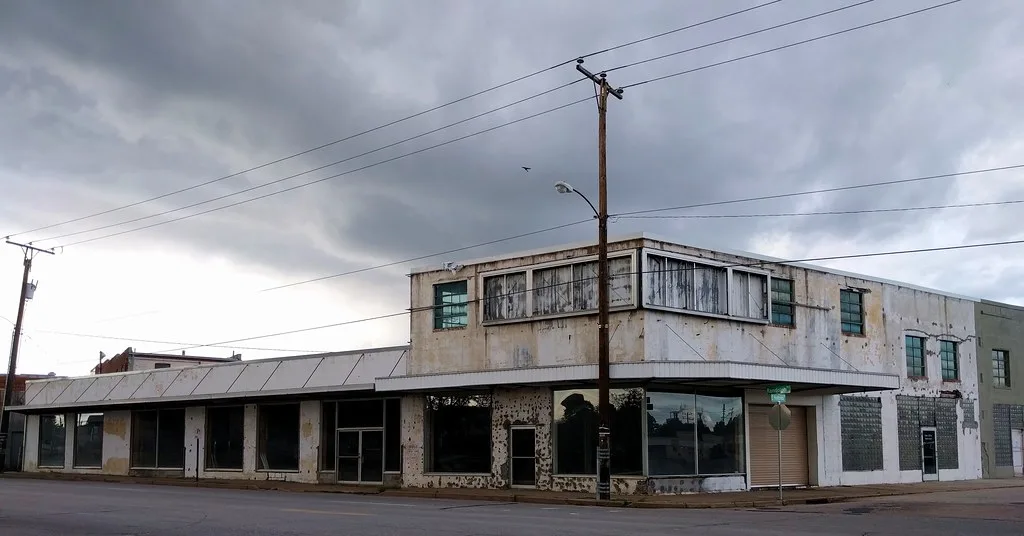 Former corner commercial building with empty shopfronts and peeling paint.