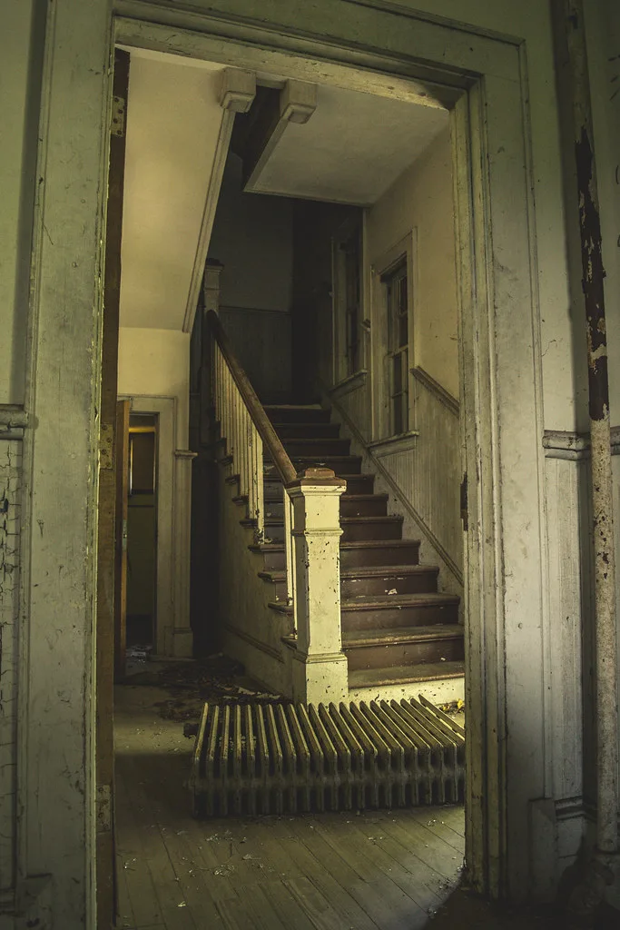 Wooden staircase with peeling paint behind a radiator lying on the floorboards.