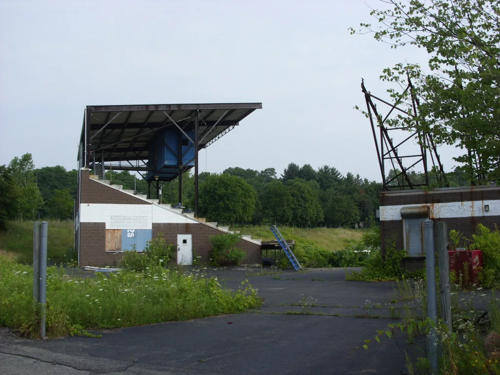 Anciennes installations de loisirs avec structures métalliques dénudées et allée envahie de végétation.