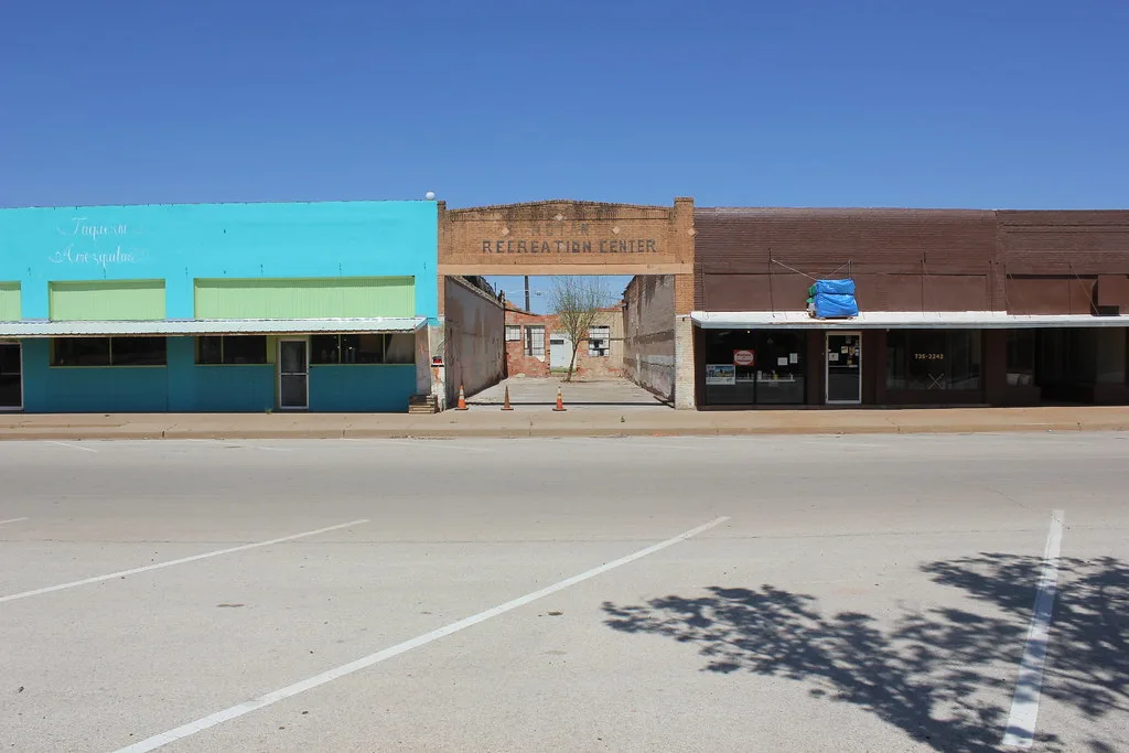 Remaining facade of a roofless former recreation center between two shops, with a tree growing inside the ruins.