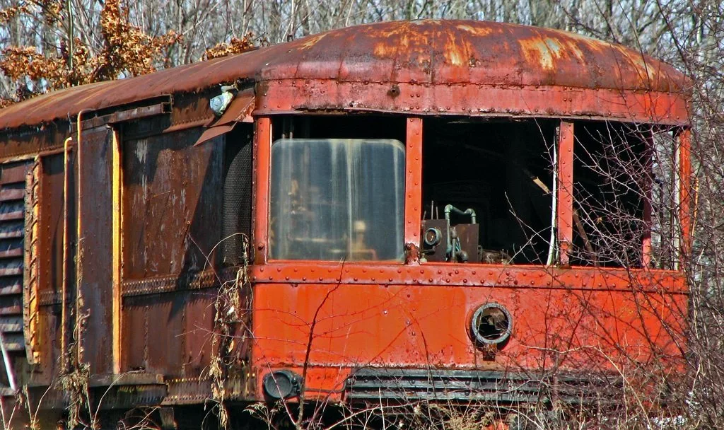Ancienne voiture ferroviaire orange rouillée parmi les broussailles.