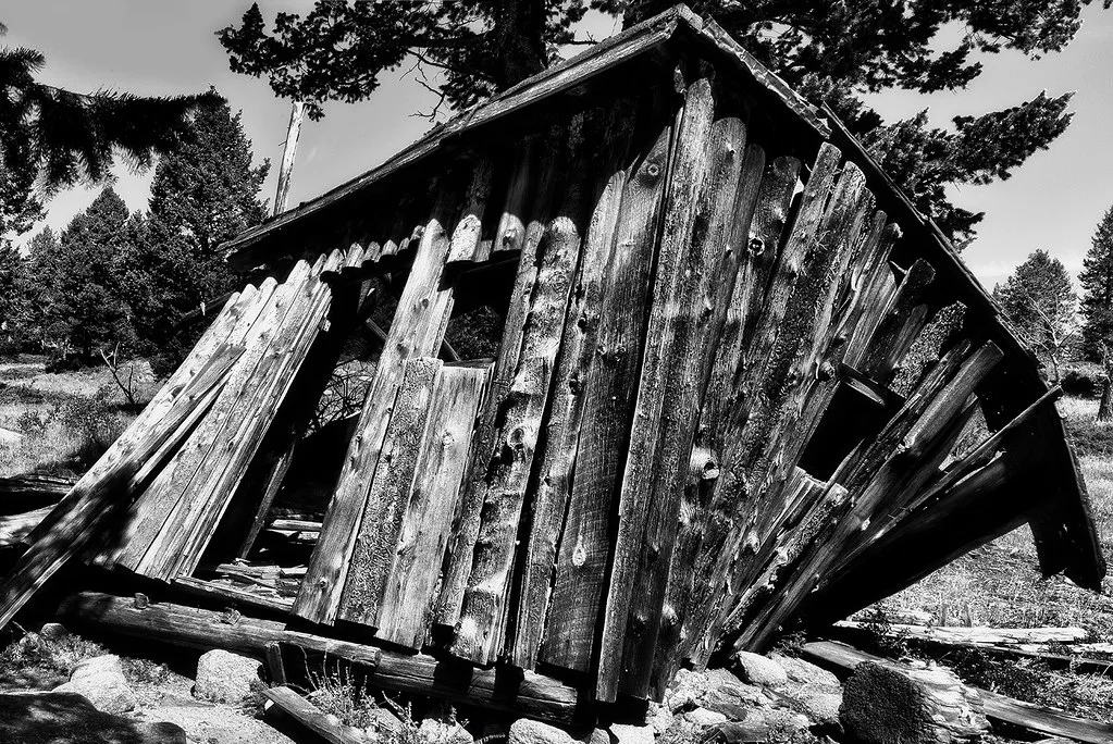 Small leaning log cabin with empty openings and separated boards.
