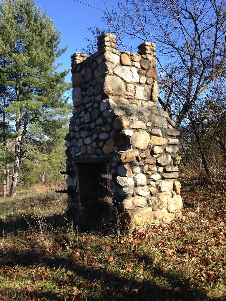 Remnant of a stone chimney on wooded ground.