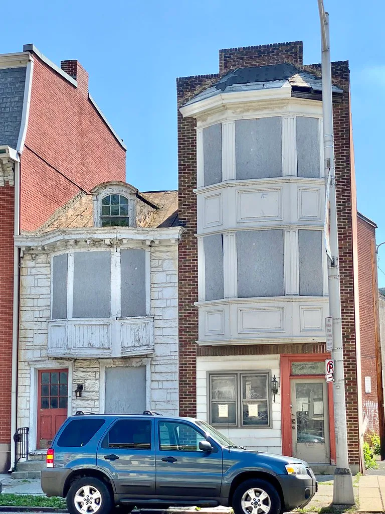 Old facades with boarded bay windows behind a blue car.