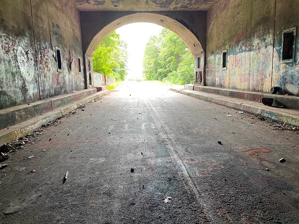 Sortie lumineuse d’un ancien tunnel routier aux murs couverts de graffitis.