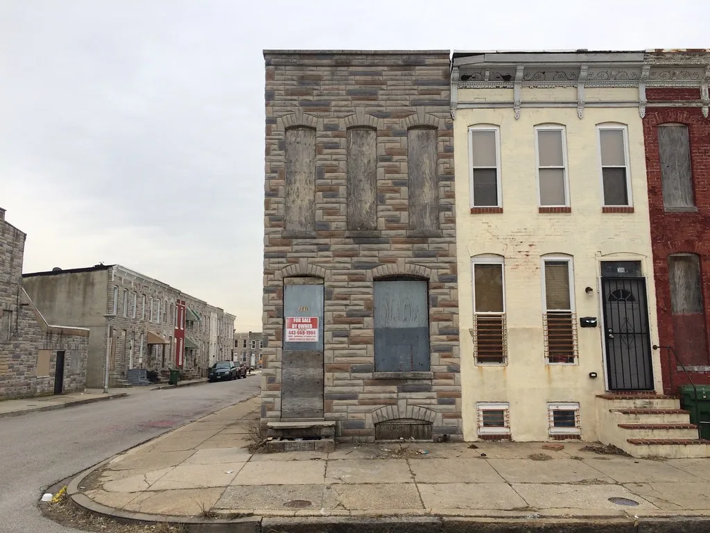 Corner house with boarded openings and deteriorated steps on an urban street.