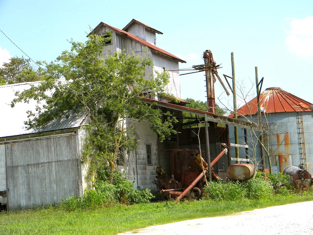 Old metal grain elevator and silo with rusty equipment in grass.