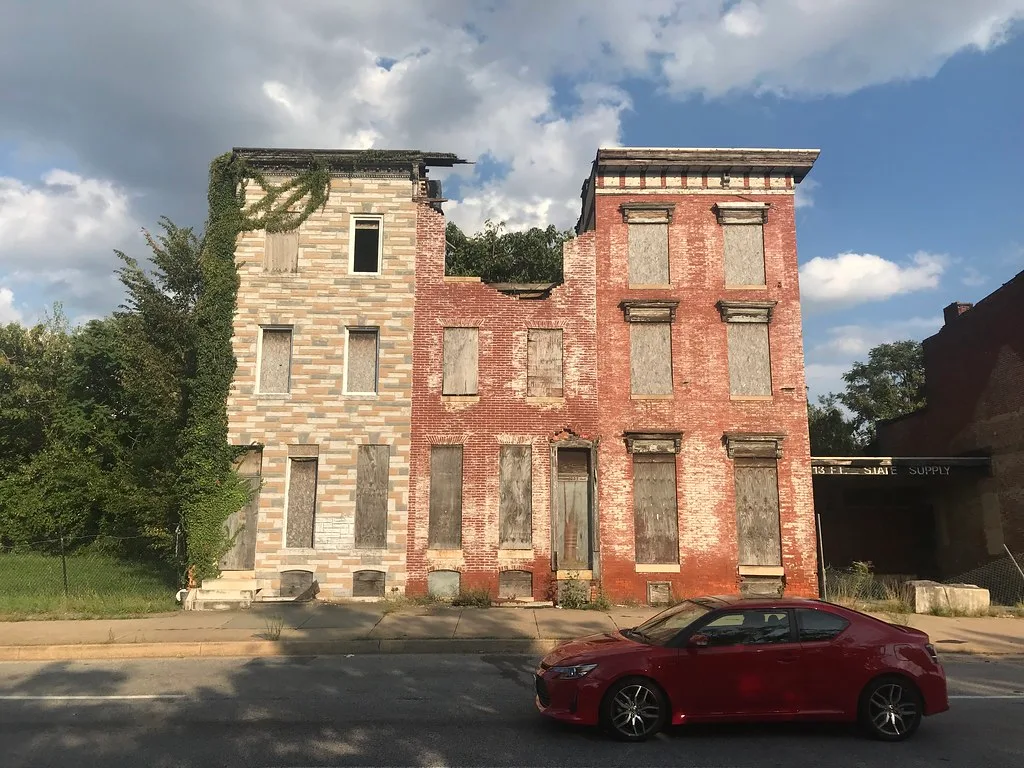 Abandoned row houses with boarded windows and a partially collapsed central facade.