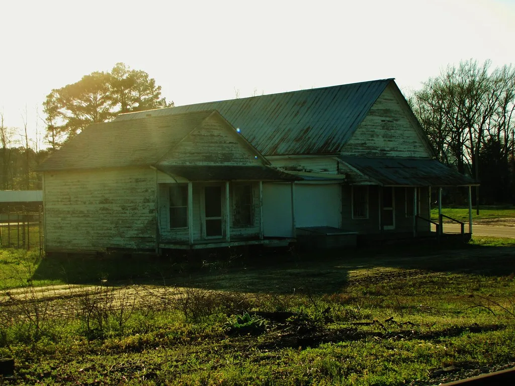 Old pale wooden building with partly boarded openings, backlit by the sun.
