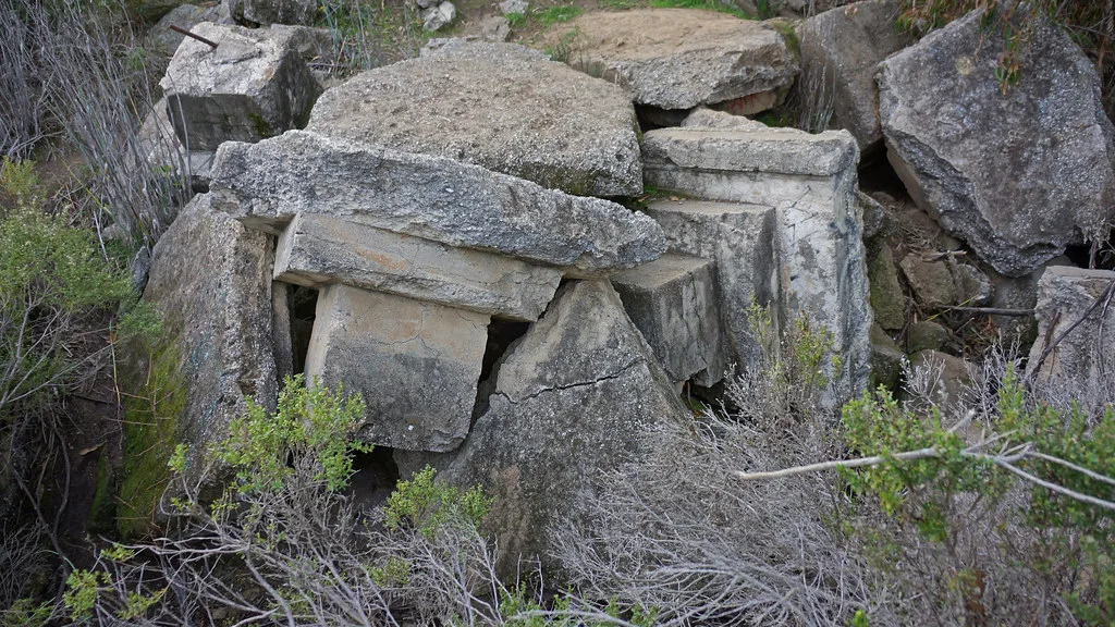 Fragments de maçonnerie moulurée et de béton brisé dans des buissons.