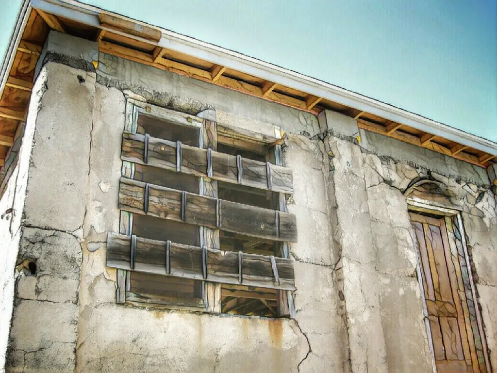 Window barred with planks and wooden door in a deeply cracked beige wall.