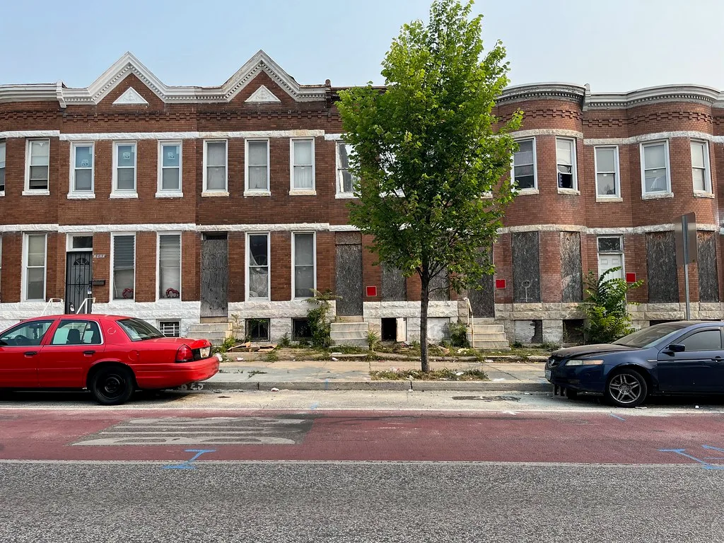 Brick row houses with boarded openings and broken panes.