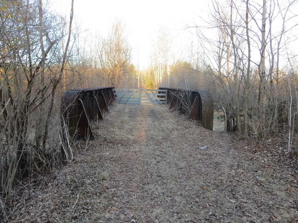 Old rusty metal bridge closed by a gate in woodland.