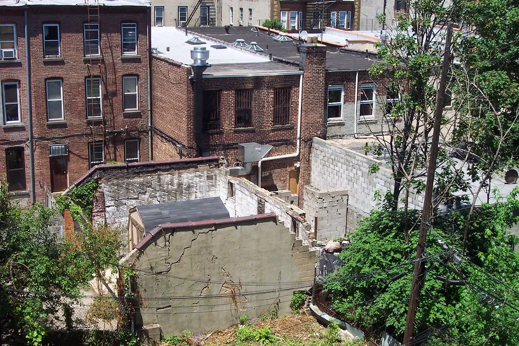 Roofless ruin with cracked walls between brick buildings.