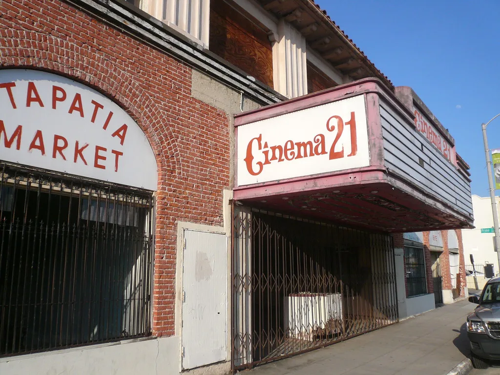 Gated entrance of an old cinema beneath a deteriorated pink marquee.