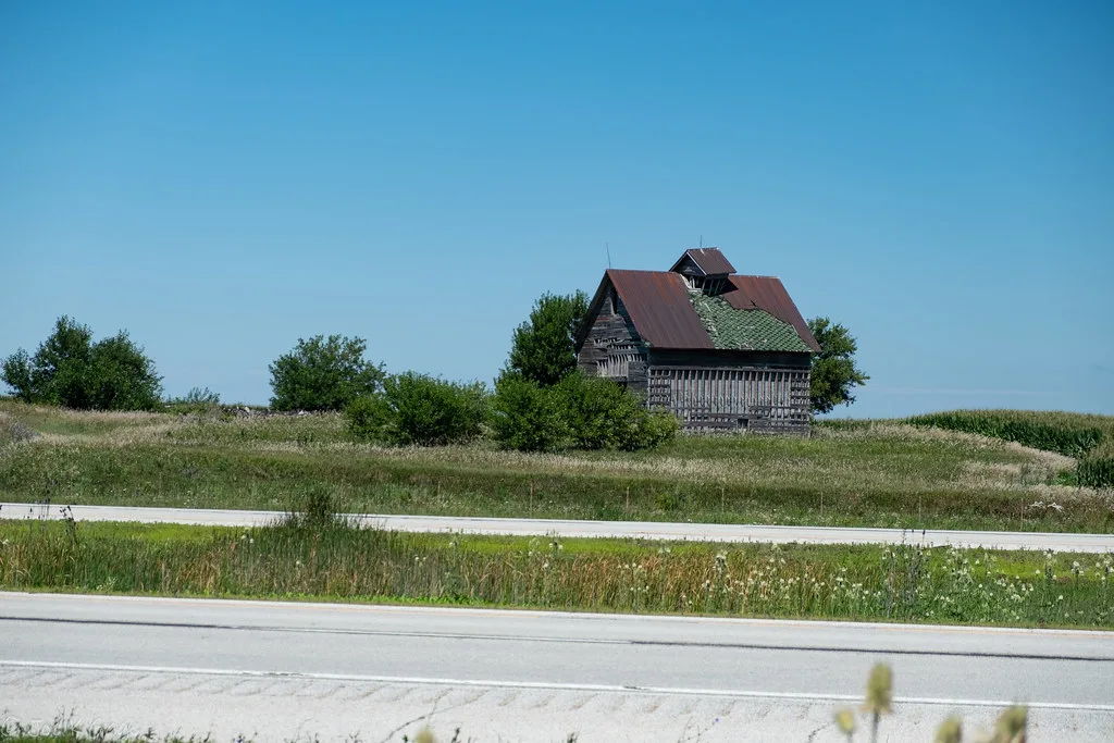Petite grange en bois à la toiture dégradée au milieu des champs.