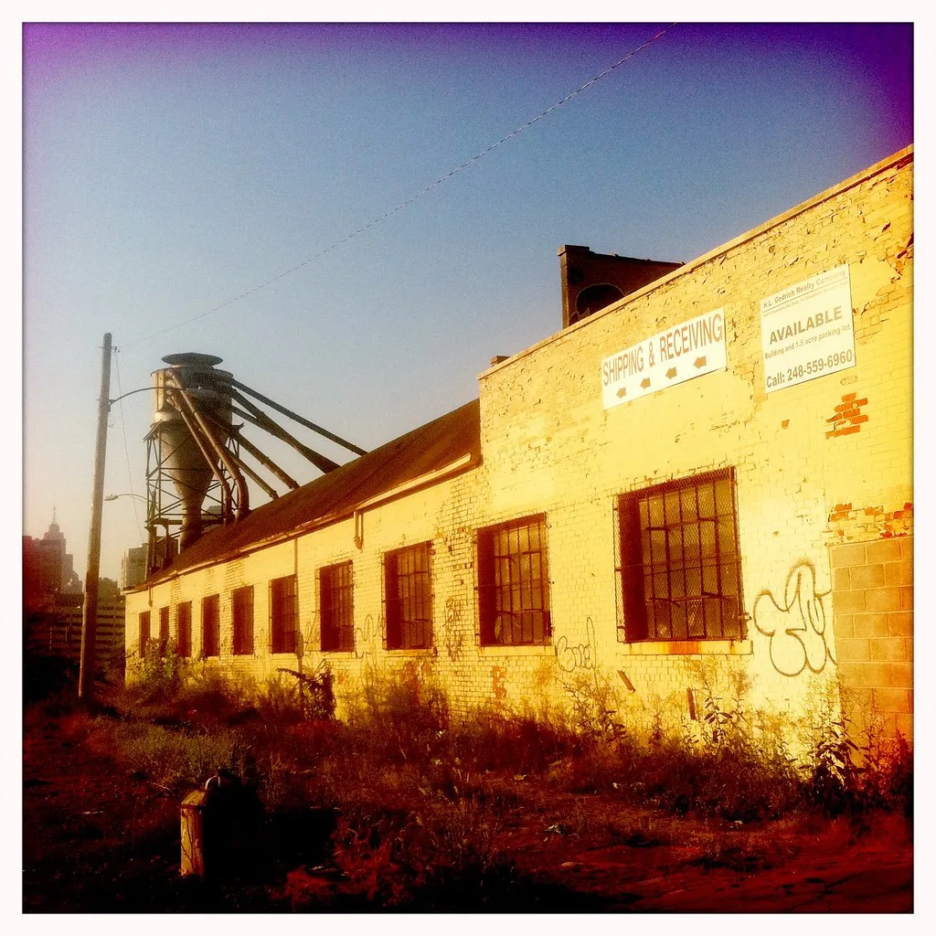 Old industrial workshop with peeling yellow walls and an overgrown yard.