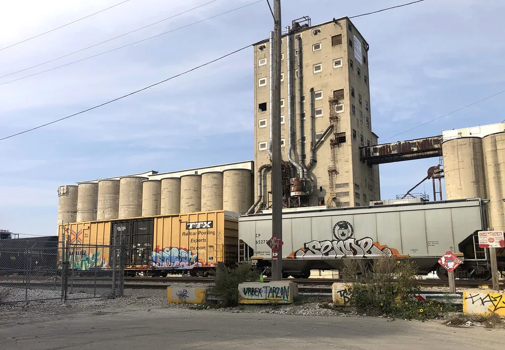 Old elevator and concrete silos behind graffiti-covered railway cars.