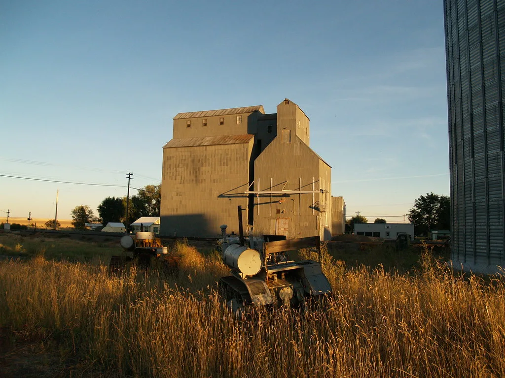 Old grain elevator with disused machinery in tall grass.