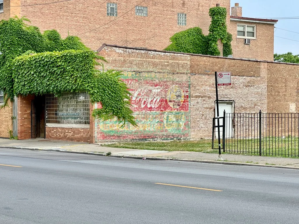 Ancien commerce en brique sur 87th Street, avec lierre et publicité murale effacée.