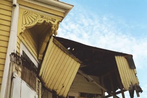 Collapsed wooden balcony on the facade of an old yellow house.