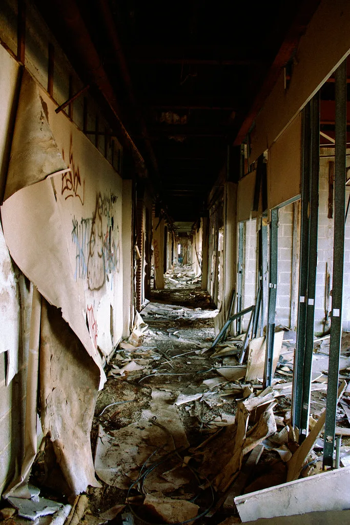 Long dark corridor with exposed partition frames and collapsed panels on the floor.