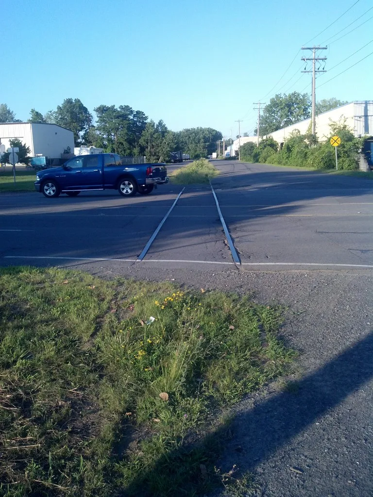 Old overgrown railway track crossing a road.