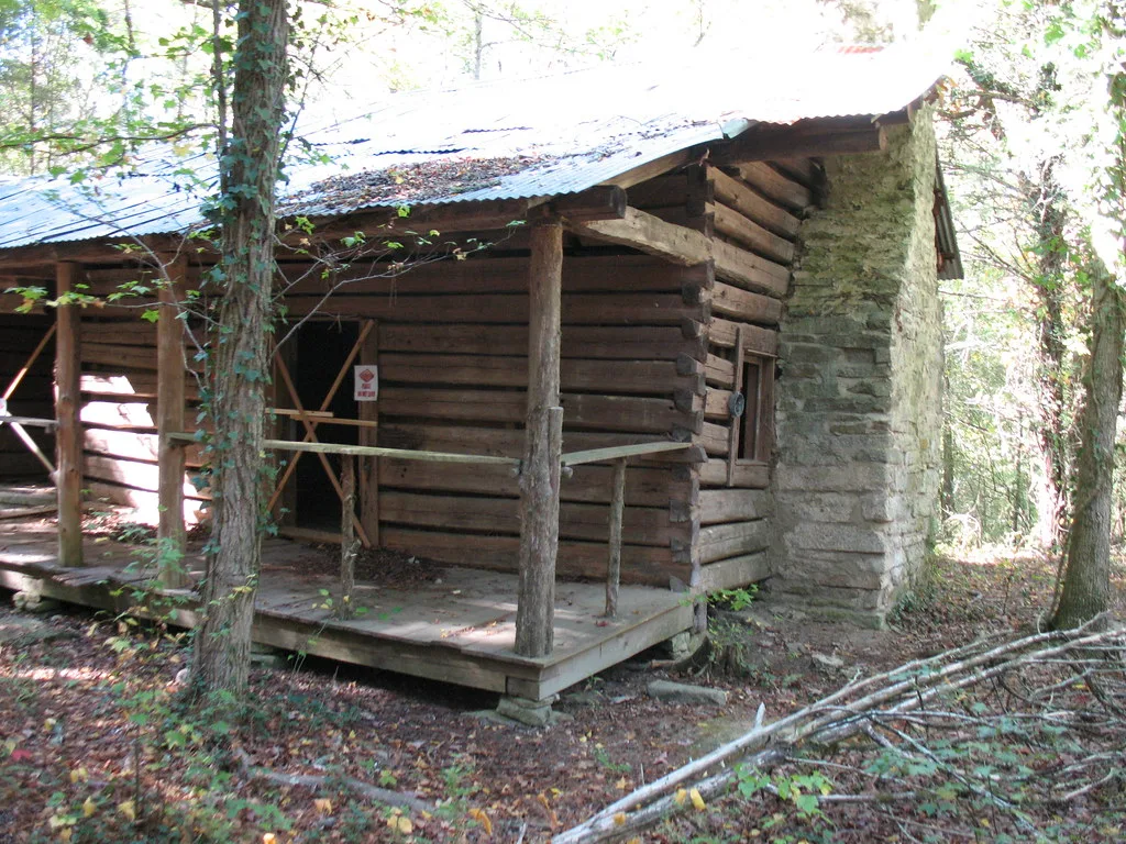 Ancienne cabane en rondins fermée avec cheminée de pierre dans les bois.