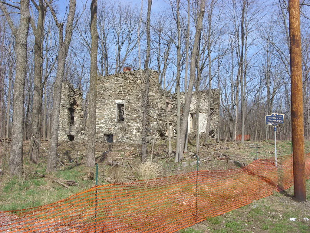 Ruins of a stone house in woodland behind a temporary fence.