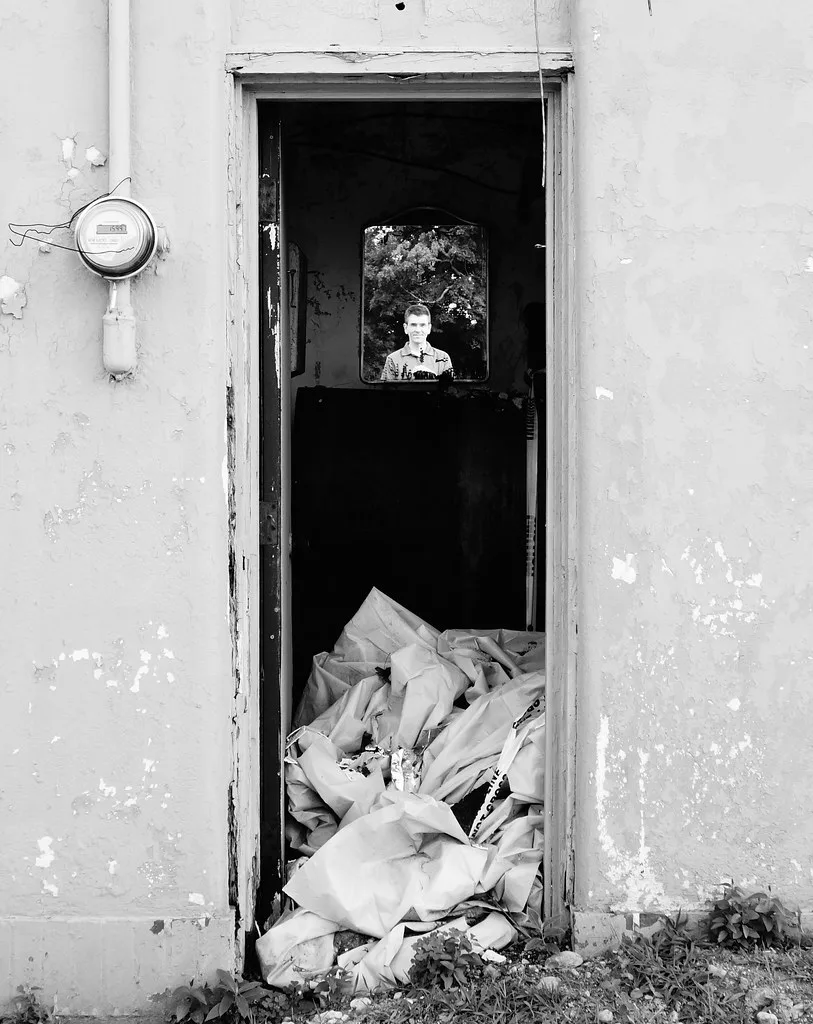 Missing doorway of a derelict building blocked by debris, with a person visible through the rear window.