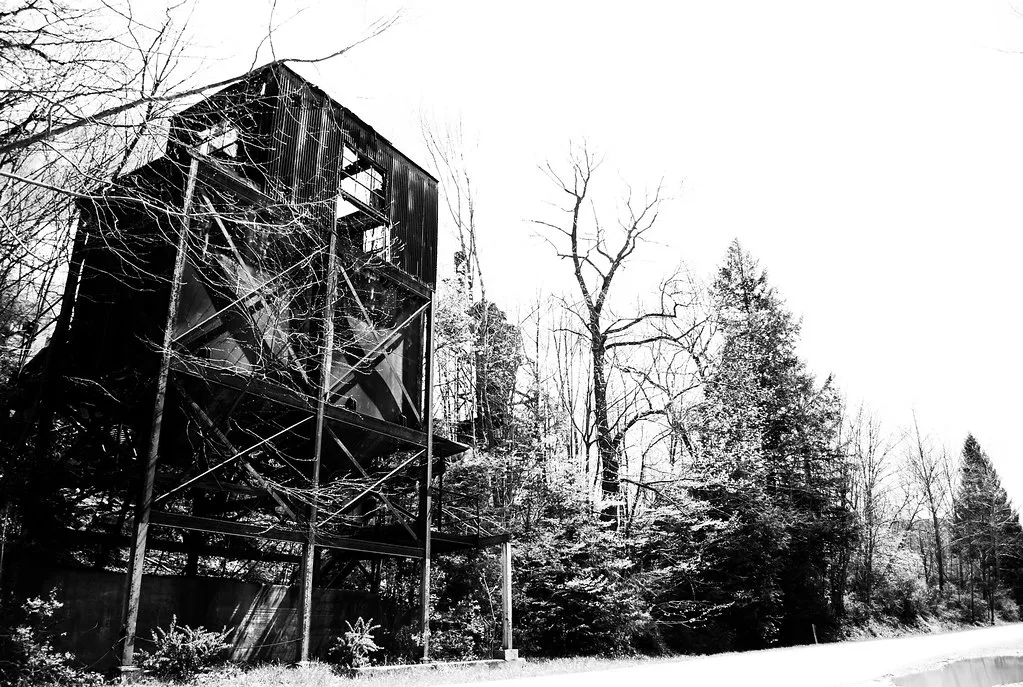 Old metal industrial structure with missing cladding among trees.