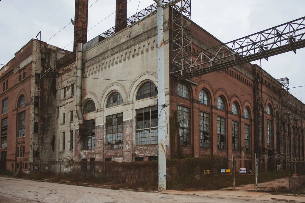 Old brick power station with large broken windows and rusty metal structures.