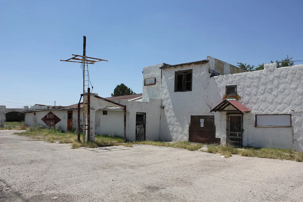 Old white building with boarded openings and a dismantled sign.