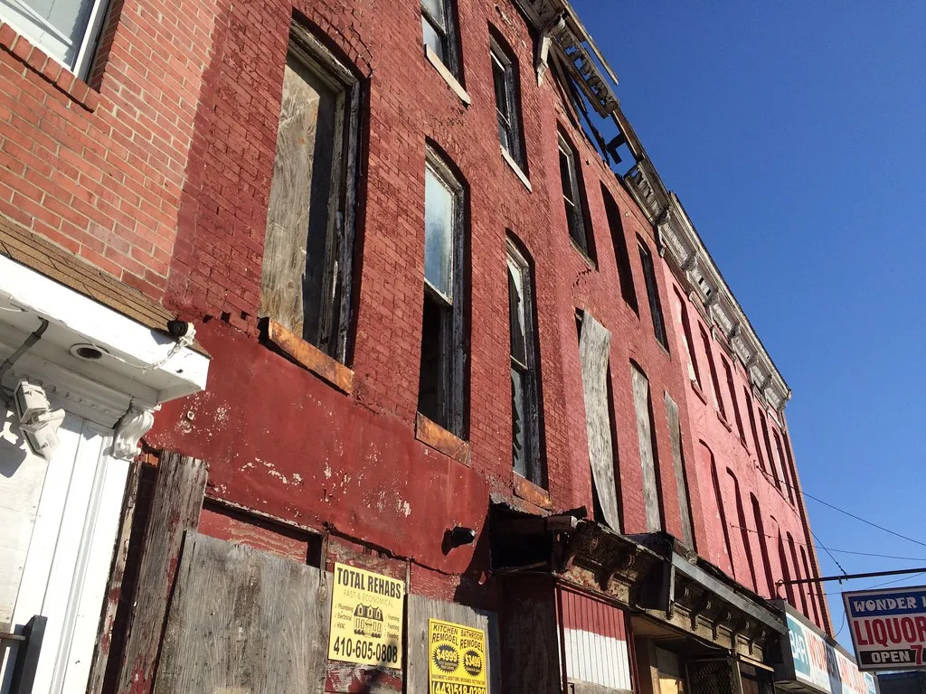 Red building with boarded windows and a deteriorated cornice.