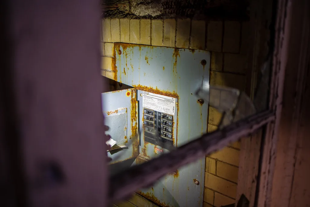Rusty electrical panel seen through a broken window.