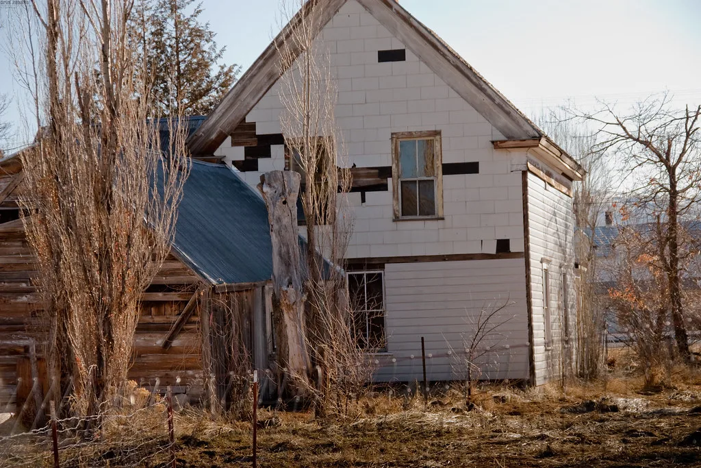 Old white house with missing siding and damaged windows.