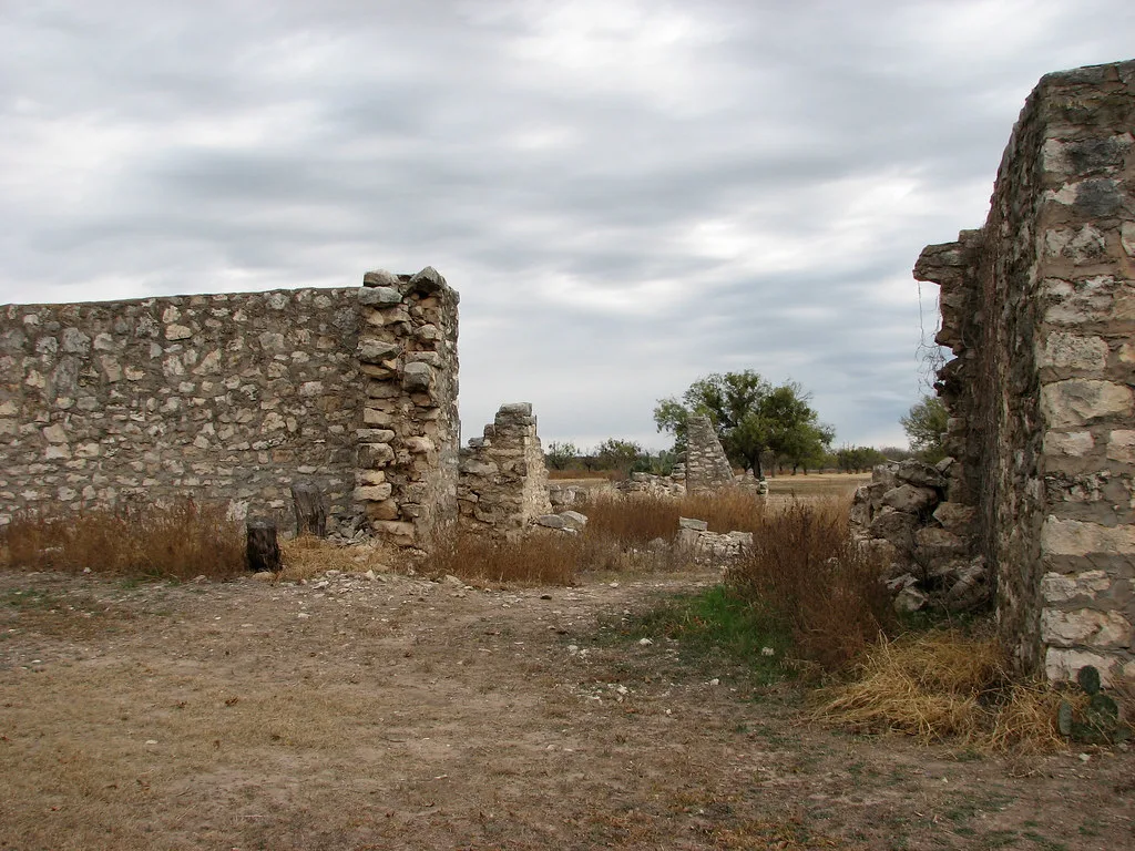 Ruined stone walls surrounded by dry grass under an overcast sky.
