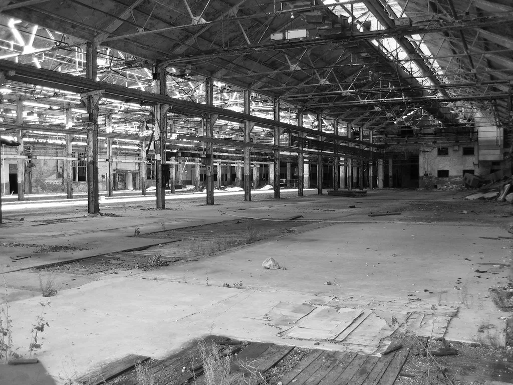 Dilapidated industrial hall with metal roof trusses, in black and white.