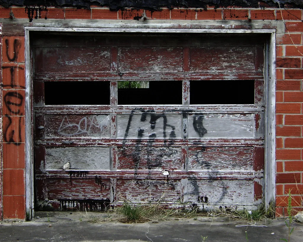 Old peeling graffiti-covered garage door with missing panes.