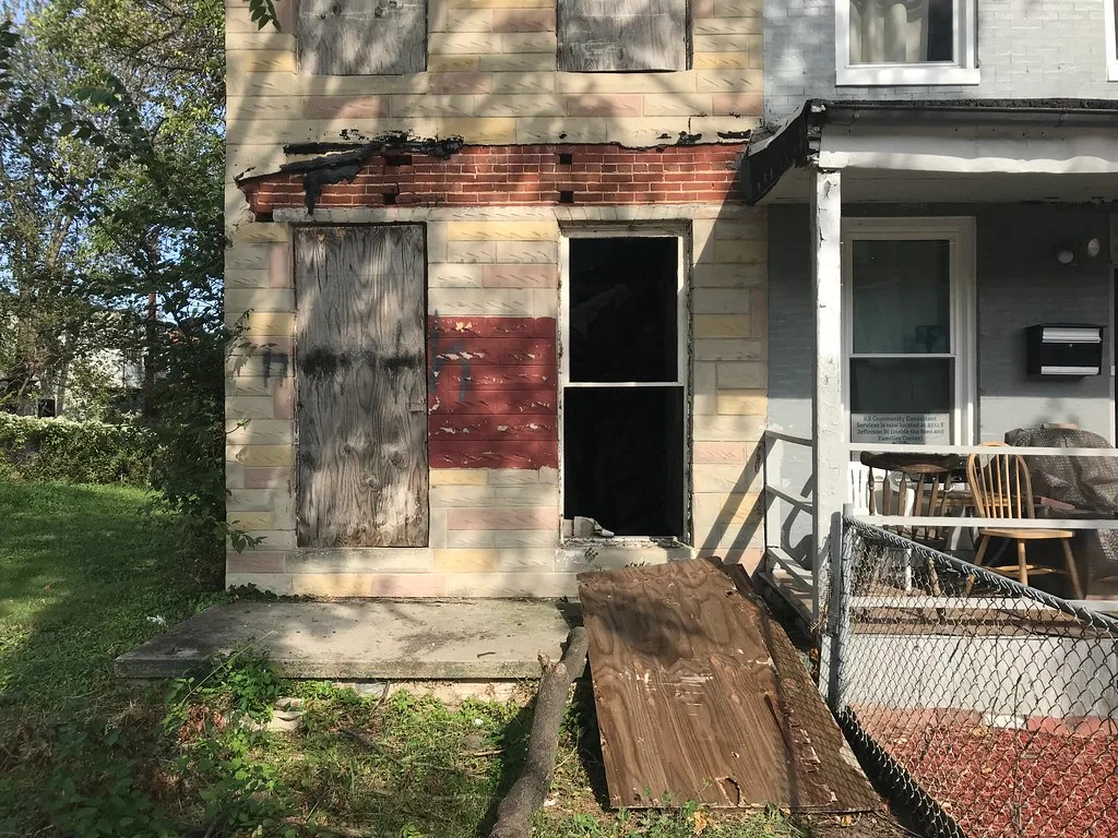 Old facade with boarded windows and an open doorway without a door.