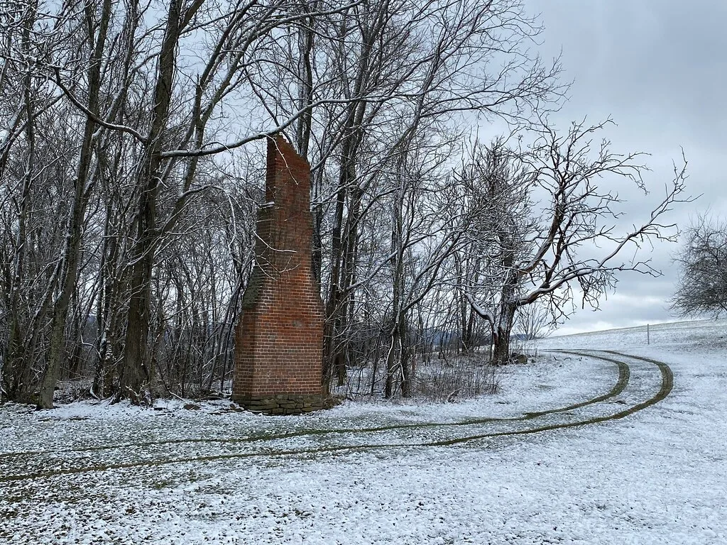 Isolated brick chimney among trees in snow.