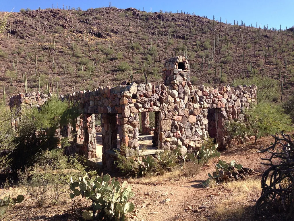 Walls and chimney of a ruined stone house among cacti.