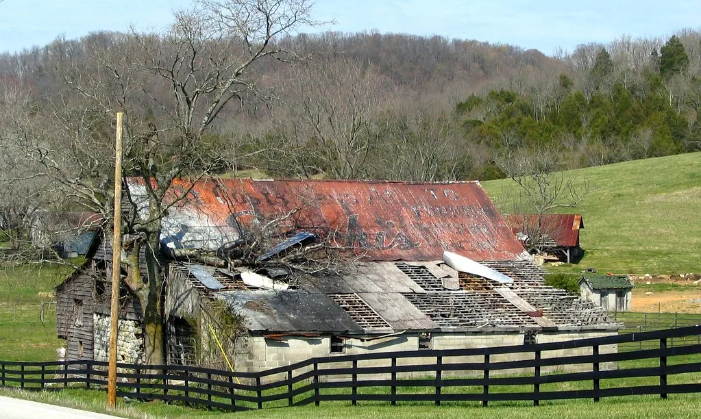 Old rural building with a collapsed roof behind a black fence.