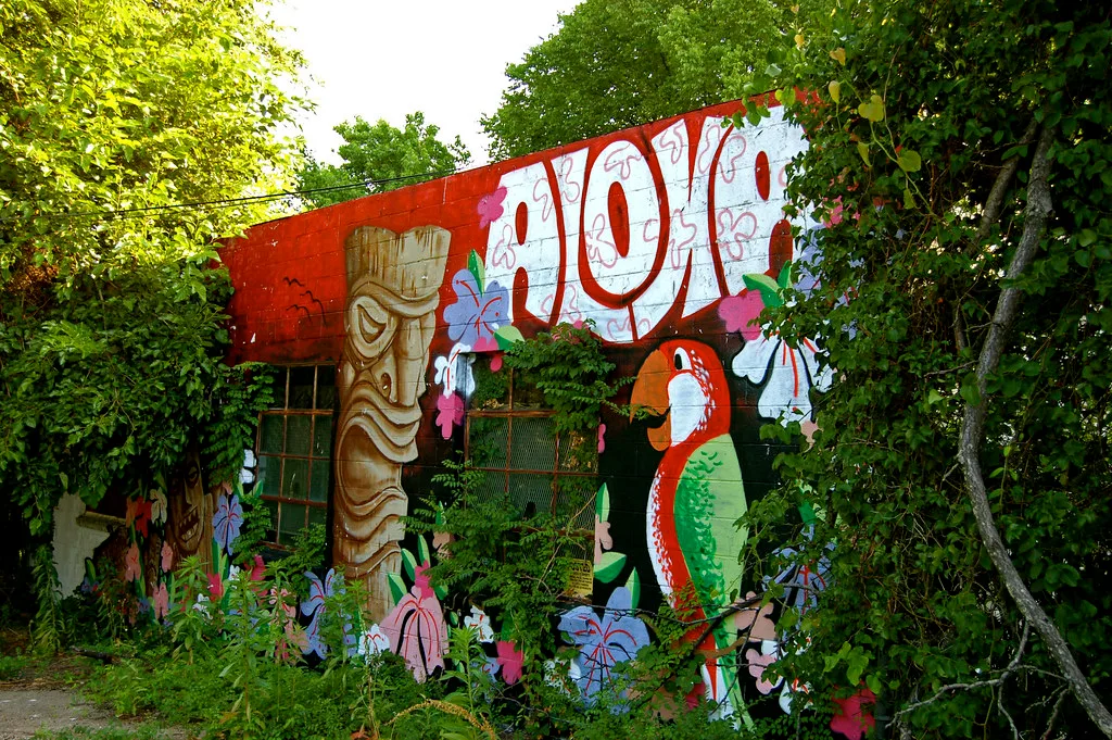 Old facade painted with tropical motifs and overgrown with vegetation.