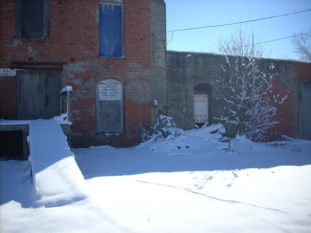 Old brick buildings with boarded doors and windows in the snow.