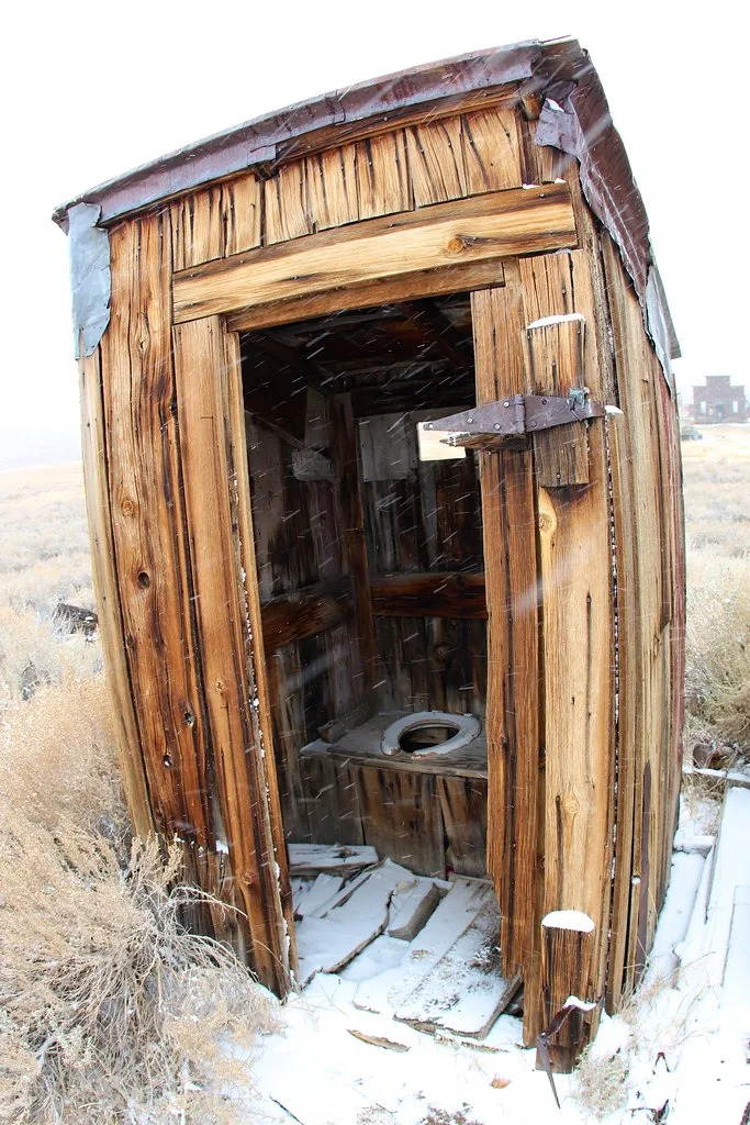 Old open and deteriorated wooden outhouse in the snow.