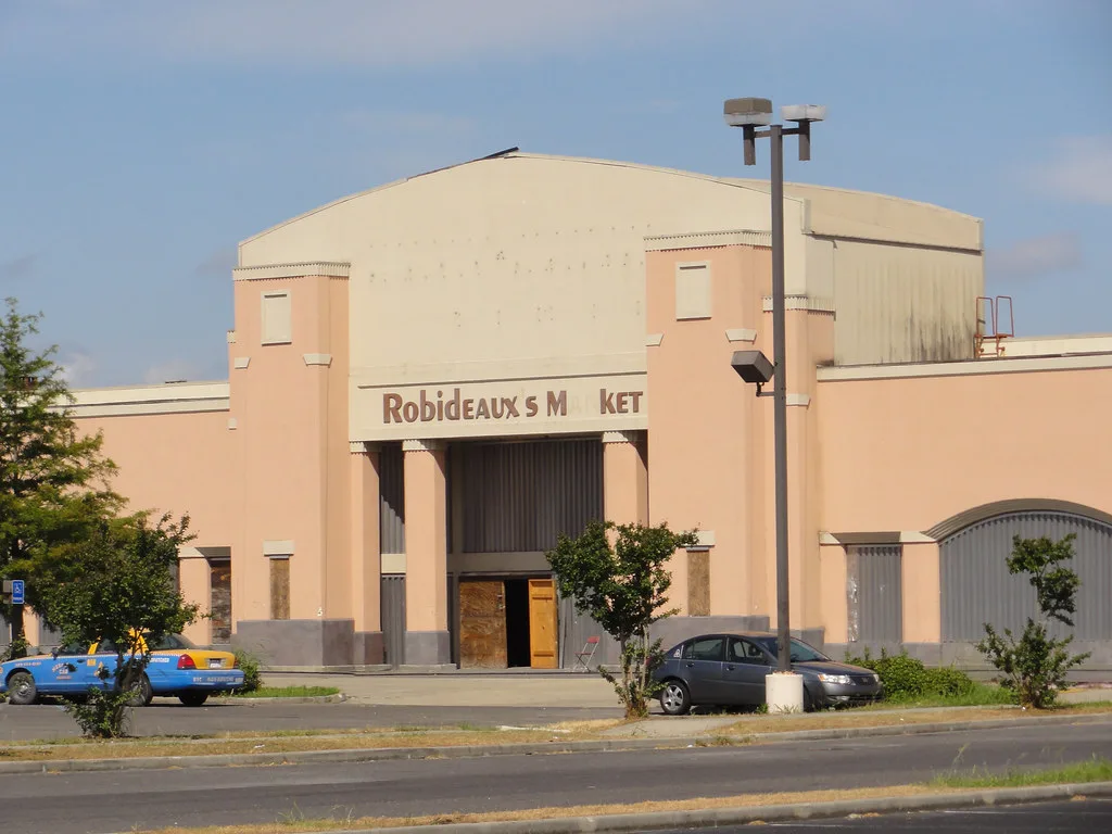 Old shop with blocked windows behind parked cars.