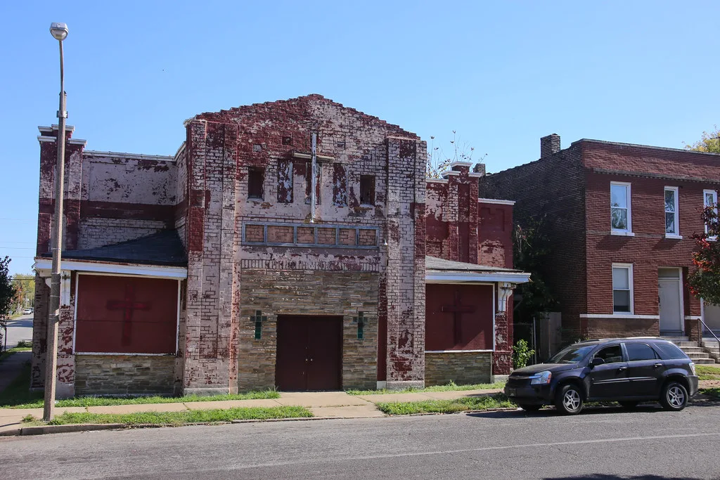 Old brick building with a flaking facade and boarded openings.