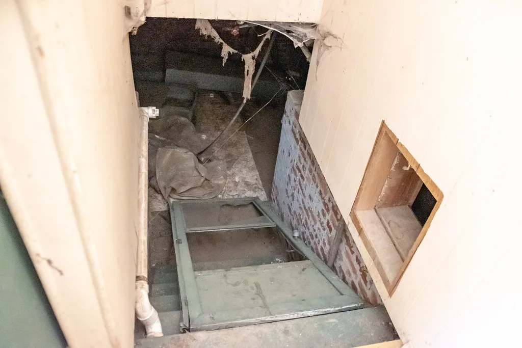 Neglected indoor staircase strewn with door panels and debris beneath cobwebs.