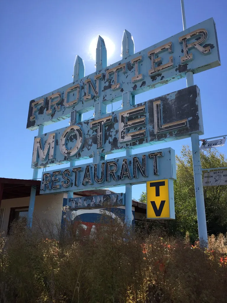 Weathered old motel sign above bushes and a boarded building.